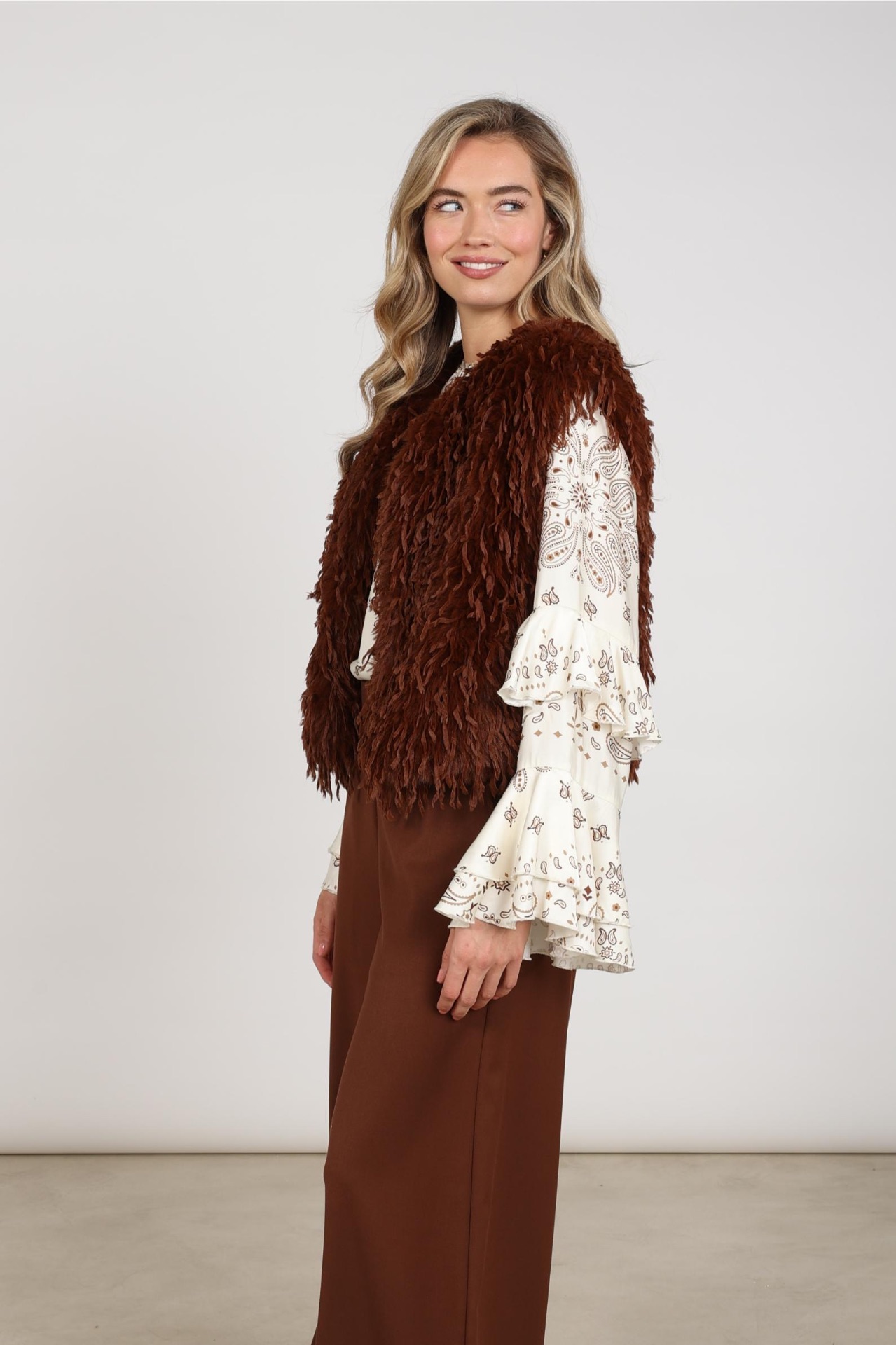 Bruine fluffy gilet van Nukus gedragen over een blouse met paisleyprint
